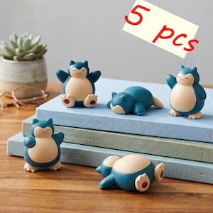 Op de afbeelding: Vijf blauwe en crèmekleurige beeldjes van een stripfiguur in verschillende poses. De beeldjes staan op een stapel boeken. De tekst "5 stuks" staat in de rechterbovenhoek.