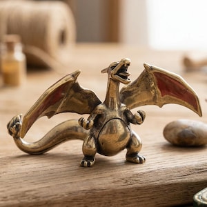 Peut inclure: Figurine de dragon en laiton avec des ailes déployées et des accents rouges. Le dragon est représenté la gueule ouverte, comme s'il rugissait. La figurine est posée sur une surface en bois.