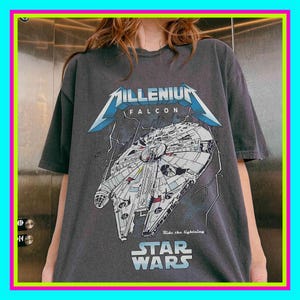 Può includere: T-shirt grigio scuro con una grafica dell'astronave Millennium Falcon di Star Wars. Il design include il testo "Millenium Falcon" e "Star Wars", con la frase "Ride the lightning".