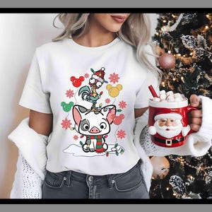 K&ouml;nnte beinhalten: Wei&szlig;es T-Shirt mit einem Cartoon-Schwein, Hahn und Mickey Mouse Ohren, verziert mit Weihnachtslichtern und Schneeflocken. Eine rote Santa-Tasse mit Marshmallows wird gehalten.