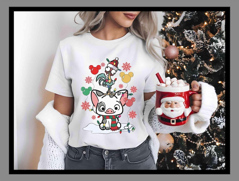 K&ouml;nnte beinhalten: Wei&szlig;es T-Shirt mit einem Cartoon-Schwein, Hahn und Mickey Mouse Ohren, verziert mit Weihnachtslichtern und Schneeflocken. Eine rote Santa-Tasse mit Marshmallows wird gehalten.