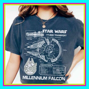 Può includere: T-shirt grigio scuro con uno schema dettagliato del Millennium Falcon di Star Wars. La maglietta include il testo "STAR WARS YT-1300 TRANSPORT" e "MILLENNIUM FALCON" in bianco. Il design è in stile blueprint.