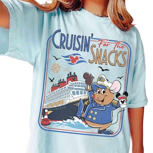Pode incluir: Camiseta azul claro com um rato de desenho animado em uniforme de capitão segurando uma xícara de café e um sorvete. A camisa tem o texto "Cruisin' For The Snacks" com um gráfico de navio de cruzeiro e orelhas do Mickey.