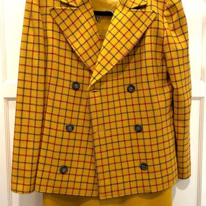 May include: A double-breasted blazer in a bright yellow fabric with a dark blue and red grid pattern, featuring wide lapels and six dark buttons. The blazer is paired with a matching solid yellow skirt, and a Valentino label is visible inside.