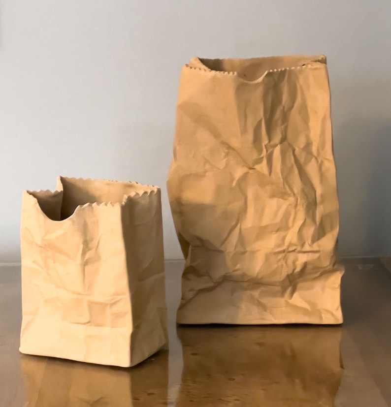 May include: Two brown paper bags of different sizes. The bags have a crinkled texture and a jagged edge at the top. One bag is taller and more upright, while the other is shorter and wider.