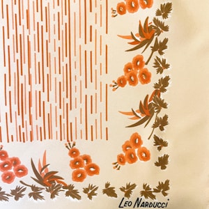May include: Cream-colored silk scarf with a design featuring vertical orange lines and floral patterns. The floral border includes orange flowers and brown leaves. The scarf is signed "Leo Narducci".
