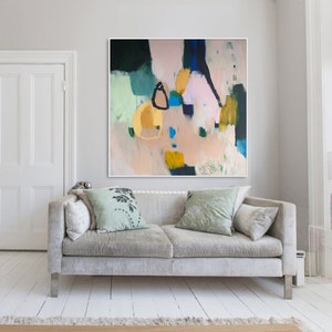 Può includere: Dipinto astratto con colori rosa, blu, verde e giallo su una tela. Il dipinto è appeso a una parete bianca sopra un divano grigio con cuscini.