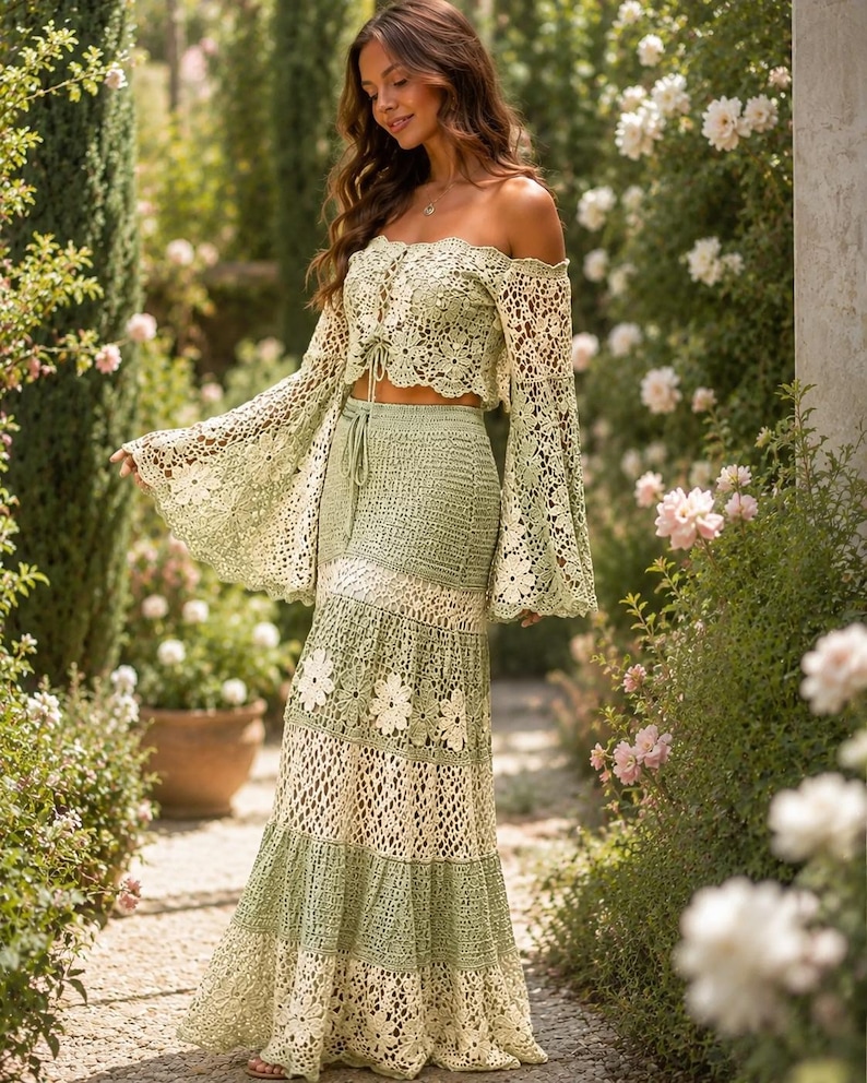 K&ouml;nnte beinhalten: Ein zweiteiliges H&auml;kel-Outfit in einem sanften Gr&uuml;nton. Das schulterfreie Oberteil hat lange, ausgestellte &Auml;rmel, und der Rock hat ein gestuftes Design mit floralen Akzenten. Das Outfit ist aus zarter, offen gewebter H&auml;kelarbeit gefertigt.