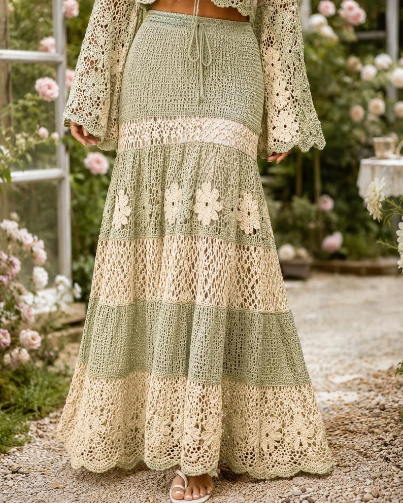 K&ouml;nnte beinhalten: Langer, flie&szlig;ender H&auml;kelrock in Salbeigr&uuml;n und Creme. Der Rock hat ein mehrschichtiges Design mit floralen Akzenten und einem gewellten Saum. Das passende Oberteil hat lange, ausgestellte &Auml;rmel. Perfekt f&uuml;r einen Bohemian- oder Resort-Stil.