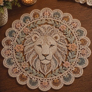 May include: A circular, cream-coloured doily with a detailed lion's head at the centre, encircled by a floral wreath. The doily has a scalloped edge with pastel accents of pink, green, and gold. The intricate crochet work is visible.