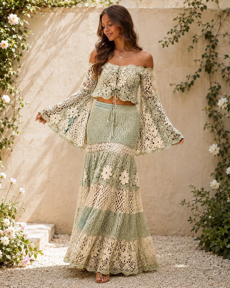 K&ouml;nnte beinhalten: Zweiteiliges H&auml;kel-Outfit in weichem Gr&uuml;n und Creme. Das schulterfreie Oberteil hat lange, ausgestellte &Auml;rmel. Der Rock ist maxilang mit floralen Akzenten. Das Outfit ist aus zarter, offen gewebter H&auml;kelarbeit.