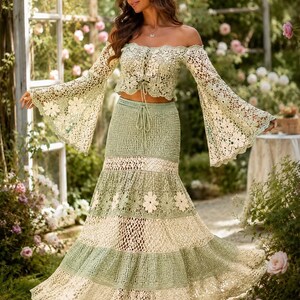 K&ouml;nnte beinhalten: Zweiteiliges H&auml;kel-Outfit in Gr&uuml;n- und Cremet&ouml;nen. Das schulterfreie Oberteil hat lange, ausgestellte &Auml;rmel und eine Bindevorderseite. Der Rock ist ein Stufen-Design mit floralen Akzenten, das eine Boho-&Auml;sthetik erzeugt.