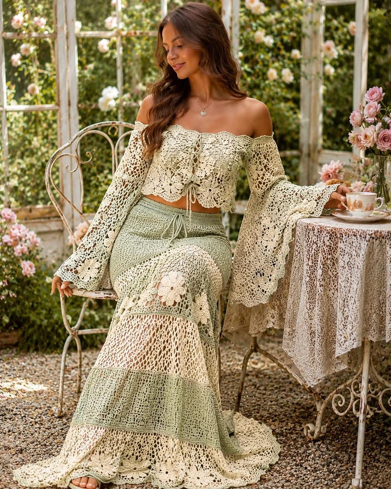 K&ouml;nnte beinhalten: Zweiteiliges H&auml;kel-Outfit in Creme und Hellgr&uuml;n. Das schulterfreie Oberteil hat lange Glocken&auml;rmel und einen Kordelzug. Der Maxirock hat ein Blumenmuster. Das Outfit wird in einem Garten getragen.