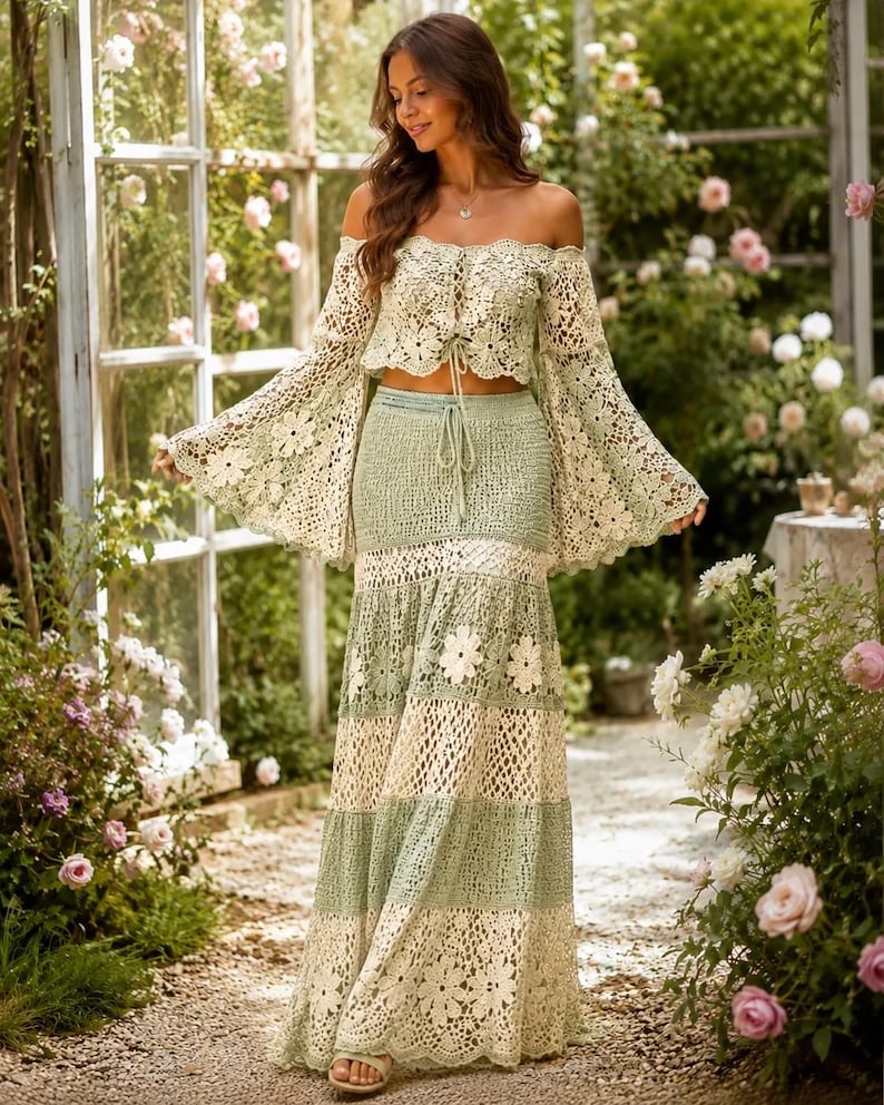 K&ouml;nnte beinhalten: Zweiteiliges H&auml;kel-Outfit in Creme und Hellgr&uuml;n. Das schulterfreie Oberteil hat lange, ausgestellte &Auml;rmel. Der Maxirock hat abwechselnde Streifen in Creme und Gr&uuml;n sowie florale Akzente. Das Outfit wird im Freien getragen.