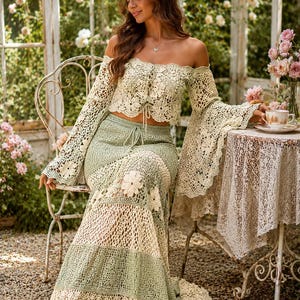 K&ouml;nnte beinhalten: Zweiteiliges H&auml;kel-Outfit in Creme und Hellgr&uuml;n. Das schulterfreie Oberteil hat lange Glocken&auml;rmel und einen Kordelzug. Der Maxirock hat ein Blumenmuster und einen Kordelzug in der Taille. Das Outfit wird im Freien getragen.