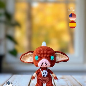 May include: A handmade crochet doll in shades of brown, tan, and white, with turquoise eyes and a skull pendant. The doll has large ears and a small white horn. The image includes the text "PDF PATTERN" and flags for the United States and Spain.