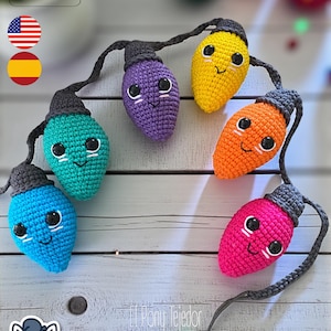May include: A string of colorful, crocheted Christmas lights with smiling faces. The lights are in shades of blue, teal, purple, yellow, orange, and pink. Each light has a gray base and a black cord. The image includes the text "PDF PATTERN".