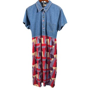 Peut inclure: Robe en jean avec manches courtes et col chemise. Le corsage est en jean bleu clair, et la jupe présente un motif patchwork avec des formes géométriques rouges, violettes et beiges. La robe a une fermeture boutonnée et une petite poche.