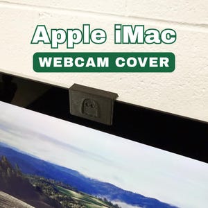 May include: A black webcam cover with a ghost design is attached to the top of a computer monitor. The text "Apple iMac" and "WEBCAM COVER" are displayed in green above the monitor.