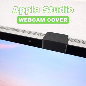 Könnte beinhalten: Eine schwarze Webcam-Abdeckung ist oben an einem Computermonitor befestigt. Der Monitor ist silberfarben und hat einen schwarzen Rand. Der Text "Apple Studio" und "Webcam Cover" sind grün dargestellt.