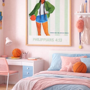 Op de afbeelding: Een slaapkamer met een roze en blauw kleurenschema. Een ingelijste print met de tekst "I CAN DO ALL THINGS... PHILIPPIANS 4:13" hangt boven een bed met blauwe en roze beddengoed. Een basketbalvormig kussen en een basketbal liggen op het bed en het bureau.