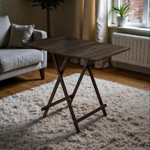 May include: A dark brown, rectangular folding table with a wood grain finish. The table has a brown, X-shaped leg design. The table is approximately 61 cm long and 41 cm wide. The table is set on a shaggy, light-coloured rug.