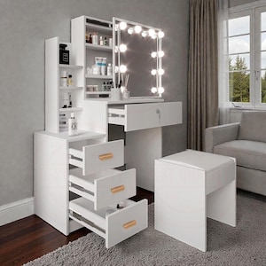 May include: A white dressing table set with a lighted mirror, drawers, and a matching stool. The vanity unit has multiple shelves and drawers with wooden handles. The mirror is framed with lights. The set is designed for a bedroom or dressing area.