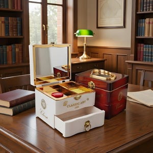 Może przedstawiać: Białe pudełko na biżuterię ze złotymi wykończeniami i szufladą, z napisem "Classic Art 1900", stoi otwarte na drewnianym stole. Obok znajduje się czerwone i złote pudełko. Tło obejmuje półki z książkami i zieloną lampę biurkową.