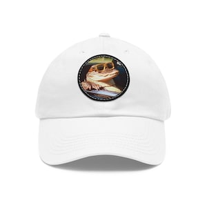 Può includere: Cappellino da baseball bianco con una toppa rotonda raffigurante un alligatore con occhiali da sole gialli. L'alligatore è marrone e beige. La toppa è bordata in bianco e nero. Il cappellino è realizzato in un materiale morbido e resistente.