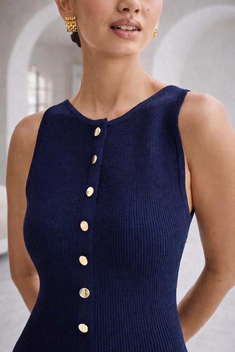 May include: A sleeveless navy blue knit top with a scoop neckline and a row of gold-colored buttons down the front. The top has a ribbed texture and a fitted silhouette, suitable for various occasions.