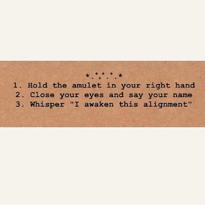 May include: A rectangular tan card with black text that reads: 1. Hold the amulet in your right hand 2. Close your eyes and say your name 3. Whisper "I awaken this alignment". Above the text is a small decorative row of stars and plus signs.