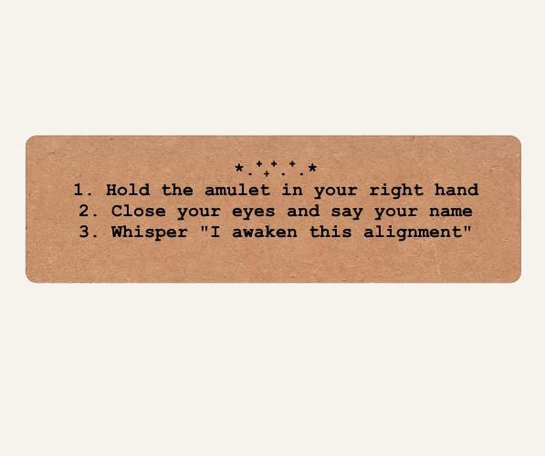 May include: A rectangular tan card with black text that reads: 1. Hold the amulet in your right hand 2. Close your eyes and say your name 3. Whisper "I awaken this alignment". Above the text is a small decorative row of stars and plus signs.