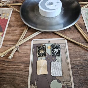 May include: Four rectangular metal charms featuring sun and moon celestial designs. Two charms have black enamel detailing with gold and silver-toned metal, while the other two are plain, textured gold and silver-toned metal rectangles.