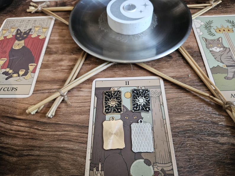 May include: Four rectangular metal charms featuring sun and moon celestial designs. Two charms have black enamel detailing with gold and silver-toned metal, while the other two are plain, textured gold and silver-toned metal rectangles.
