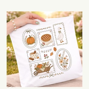 May include: A white square pillow cover featuring a series of framed illustrations including a pumpkin, a lattice-top pie, a goose, a mug with cinnamon sticks, a bouquet of flowers, and a wheelbarrow filled with pumpkins and gourds.