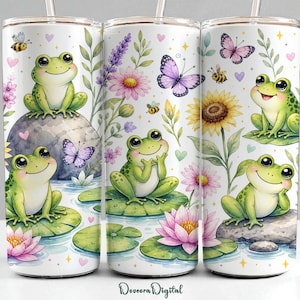 May include: White tumbler featuring a whimsical design of smiling green frogs, butterflies, bees, and flowers. The design includes a sunflower, water lilies, and a pond scene. The tumbler has a straw and is decorated with the text "Doveora Digital".