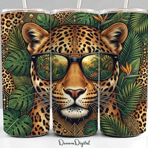 May include: A cylindrical tumbler featuring a leopard face wearing black sunglasses. The design includes a leopard print background, green tropical monstera leaves, and orange bird of paradise flowers. The sunglasses reflect a sunset jungle scene.