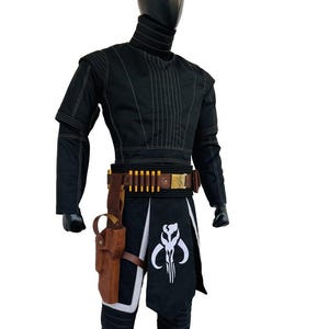 May include: Black costume with a high collar, featuring white stitching details. The outfit includes a brown belt with gold accents and a holster. A black and white graphic is on the lower garment. The costume is displayed on a mannequin.