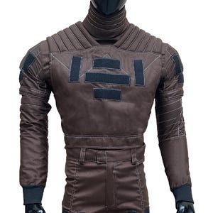 May include: A brown jumpsuit with black accents, displayed on a mannequin. The suit features a high collar, quilted detailing, and multiple black rectangular patches. White stitching outlines the seams and panels. The sleeves end with black cuffs.