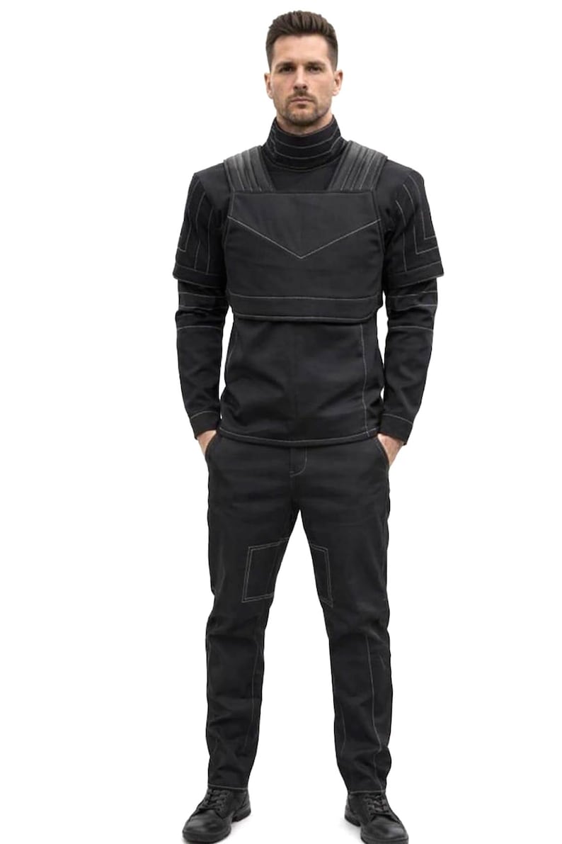 May include: A black outfit featuring a high-neck top, a vest-like overlay, and matching pants. The outfit has white stitching details and is worn with black shoes. The person is standing with their hands in their pockets.