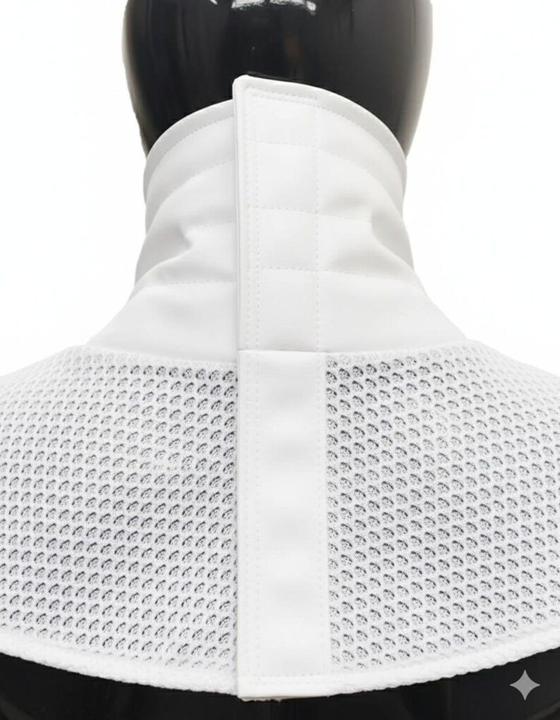 Może przedstawiać: Biały kołnierz szermierczy z siatkowym śliniakiem i wyściełanym, pionowym kołnierzem. Kołnierz posiada centralny, pionowy pasek z zapięciem na zatrzask. Siatkowy śliniak ma chronić szyję i klatkę piersiową podczas szermierki.