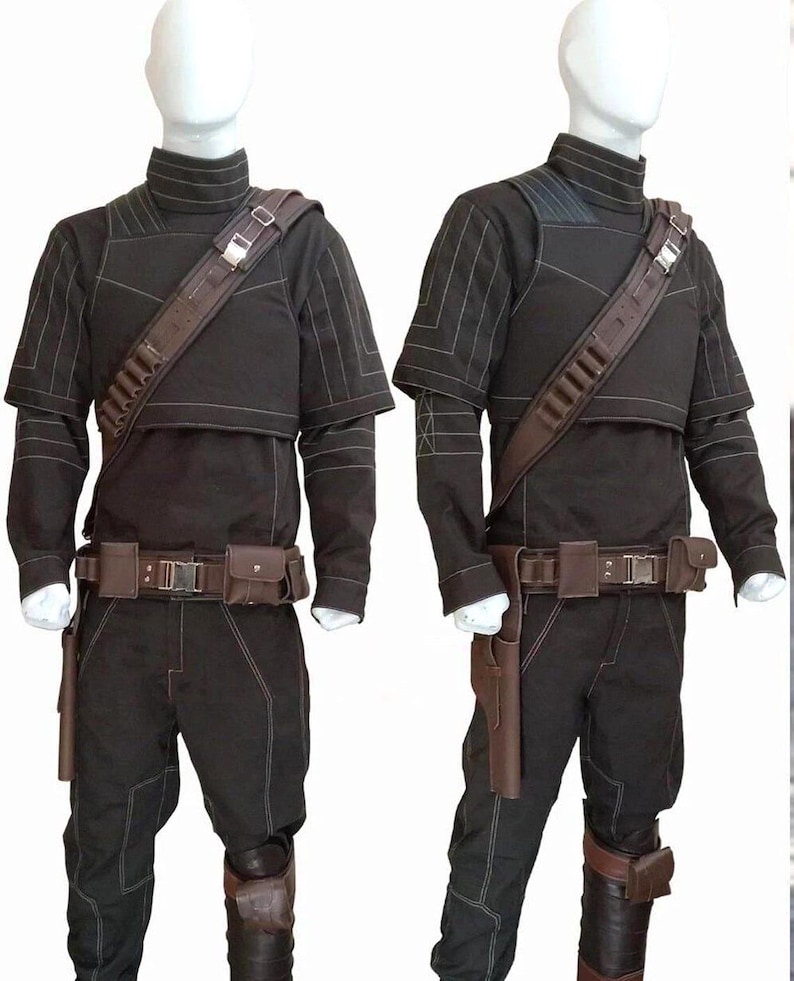 May include: Two black costumes displayed on mannequins. Each costume includes a long-sleeved top with white stitching, matching pants, a brown belt with pouches, and a shoulder strap with ammunition holders. Brown holsters and knee pads complete the look.
