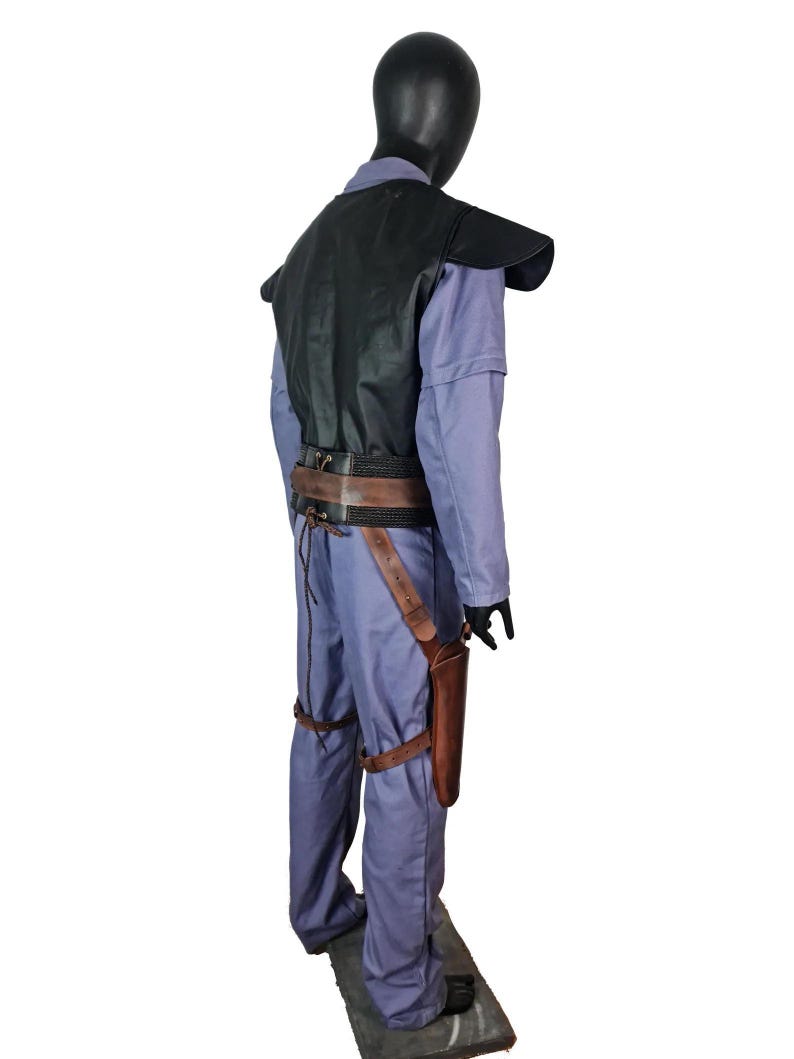K&ouml;nnte beinhalten: Ein Kost&uuml;m auf einer Schaufensterpuppe, bestehend aus einem hellblauen Overall, einer schwarzen Weste und einem braunen Lederg&uuml;rtel mit Holster. Das Kost&uuml;m umfasst braune Lederbeinriemen und schwarze Handschuhe. Die Schaufensterpuppe steht auf einer grauen Plattform.