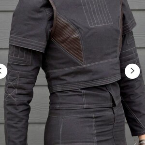 May include: Dark gray jacket and pants set with brown leather accents. The jacket features a high collar, shoulder pads, and decorative stitching. The pants are high-waisted and fitted. The outfit is made of a durable fabric, suitable for cosplay or fashion.