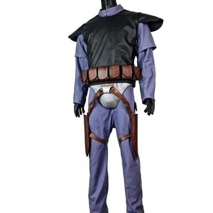 K&ouml;nnte beinhalten: Ein Kost&uuml;m, das auf einer Schaufensterpuppe ausgestellt ist. Das Kost&uuml;m umfasst einen blauen Overall, eine schwarze Weste, einen braunen G&uuml;rtel mit Taschen und braune Halfter. Die Schaufensterpuppe ist schwarz und das Kost&uuml;m wird auf einer grauen Basis pr&auml;sentiert.