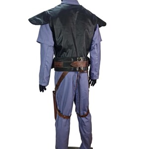 K&ouml;nnte beinhalten: Ein komplettes Kost&uuml;m, das auf einer Schaufensterpuppe pr&auml;sentiert wird. Das Kost&uuml;m umfasst einen hellblauen Overall, eine schwarze Weste und einen braunen G&uuml;rtel mit Holster. Das Kost&uuml;m hat auch braune Beingurte und schwarze Handschuhe. Die Schaufensterpuppe steht auf einem grauen Sockel.