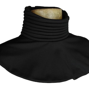 Puede incluir: Un calentador de cuello negro con un cuello alto y acanalado y una base ancha y acampanada. El cuello est&aacute; hecho de m&uacute;ltiples capas apiladas, creando una apariencia texturizada. El calentador de cuello est&aacute; dise&ntilde;ado para brindar calidez y protecci&oacute;n.