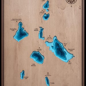 May include: Wooden wall art of Mammoth Lakes, California, USA, featuring a detailed topographic map. The map shows the lakes in shades of blue, with text labels and a compass rose. The artwork is framed in a dark brown wood.