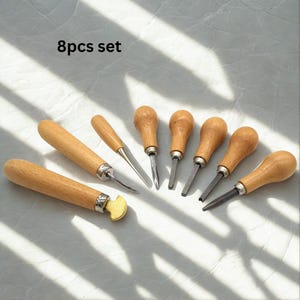 May include: A set of eight wood carving tools with wooden handles and metal blades. The tools are arranged on a light-colored surface. The text "8pcs set" is visible in the upper left corner.