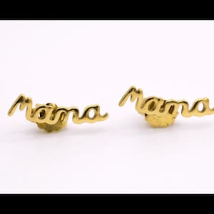 Puede incluir: Un par de pendientes dorados. Cada pendiente deletrea la palabra "Mama" en escritura cursiva. Los pendientes están sobre un fondo blanco.